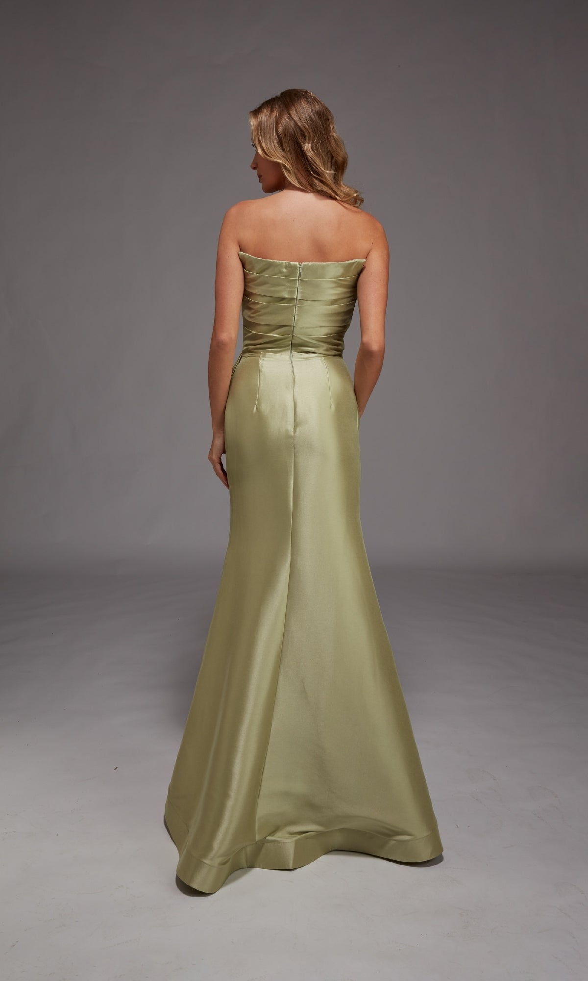 A woman faces away, wearing the Long Formal Dress: Alyce 27806—a strapless, floor-length light green mermaid gown—set against a plain gray background.